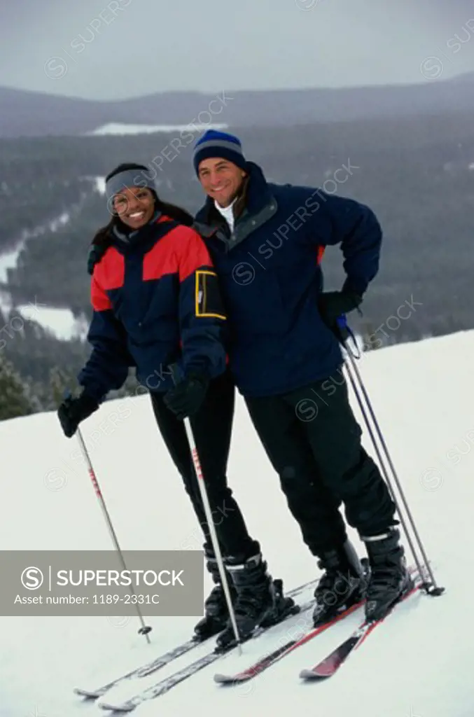Portrait of a young couple standing in snow with ski equipment