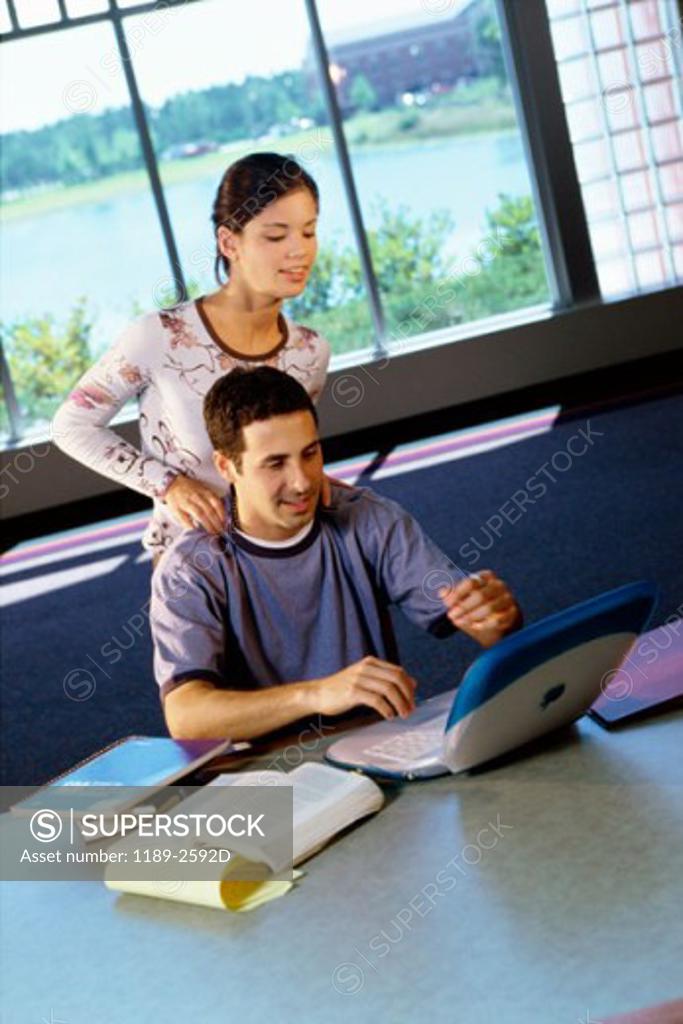 Stock Photo: 1189-2592D Teenage boy using a laptop with a teenage girl standing behind him