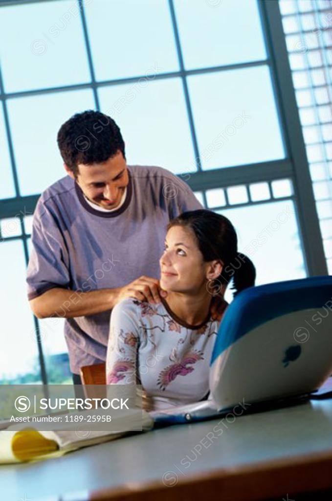 Stock Photo: 1189-2595B Teenage girl using a laptop with a teenage boy standing behind her