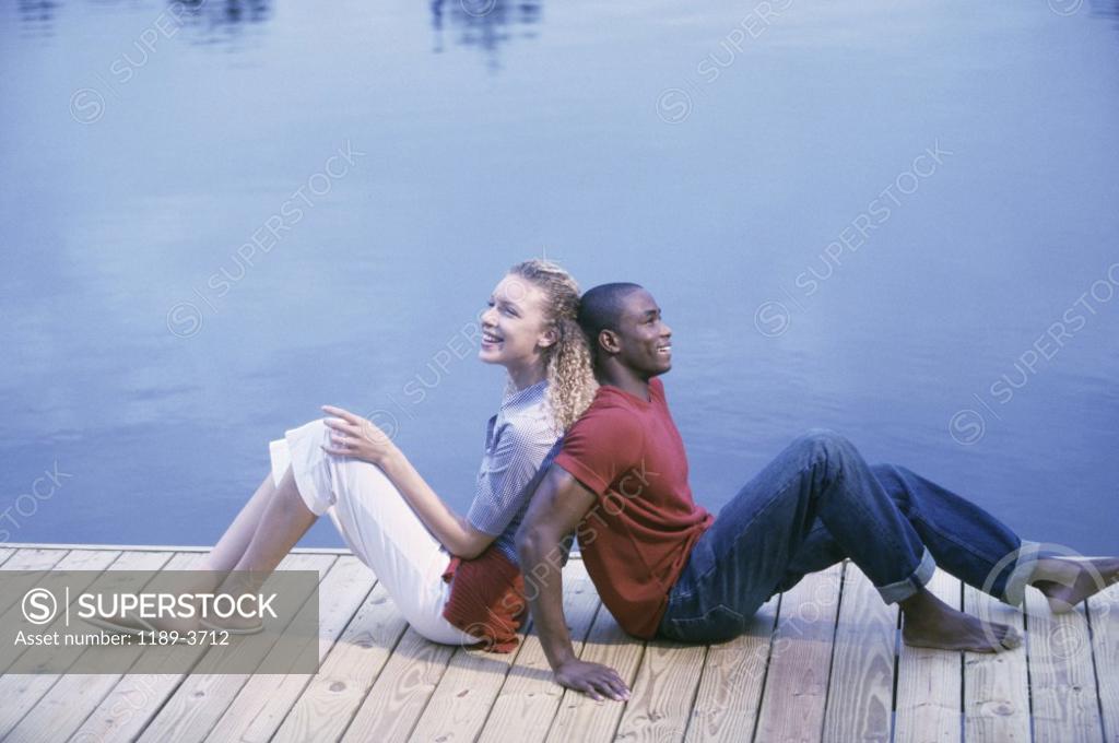Stock Photo: 1189-3712 Young couple sitting back to back beside a lake