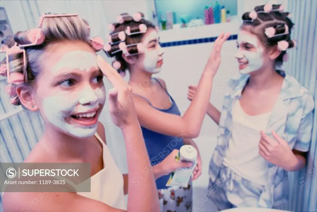 Three teenage girls wearing hair curlers and facial masks