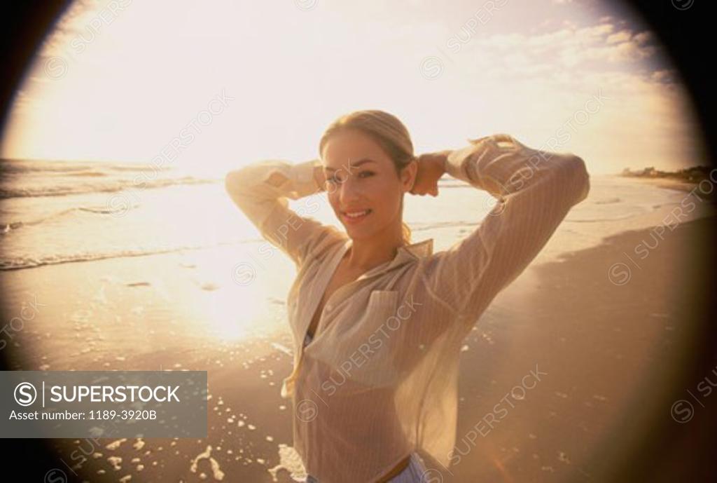 Stock Photo: 1189-3920B Young woman standing with her hands behind her head on the beach