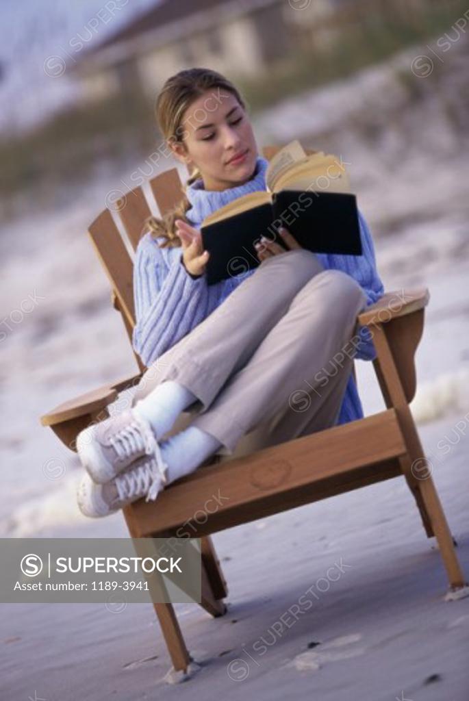 Stock Photo: 1189-3941 Young woman reading a book on the beach