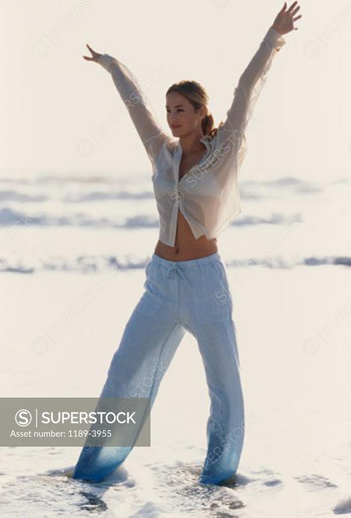 Stock Photo: 1189-3955 Young woman standing with her arms raised on the beach
