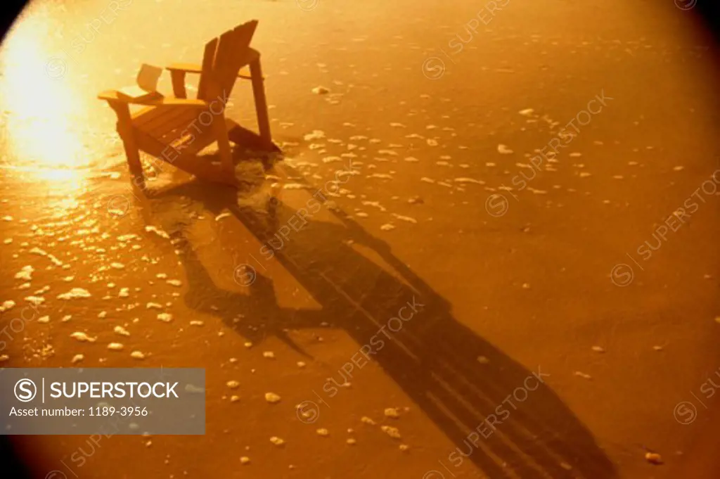 A lawn chair on a beach during sunset