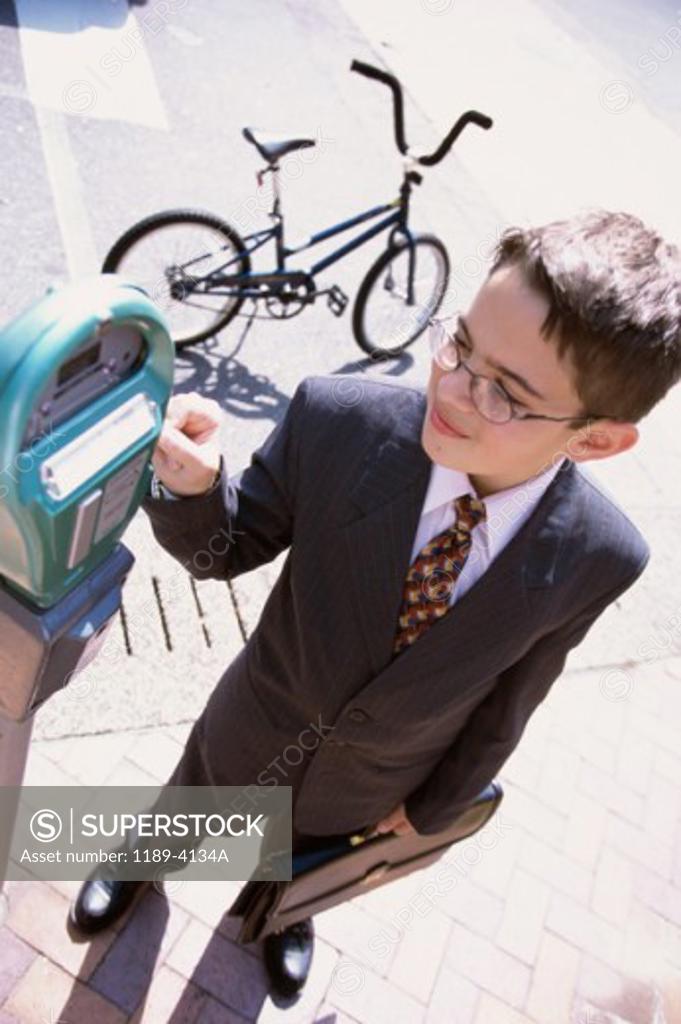 Stock Photo: 1189-4134A High angle view of a boy wearing a business suit operating a parking meter