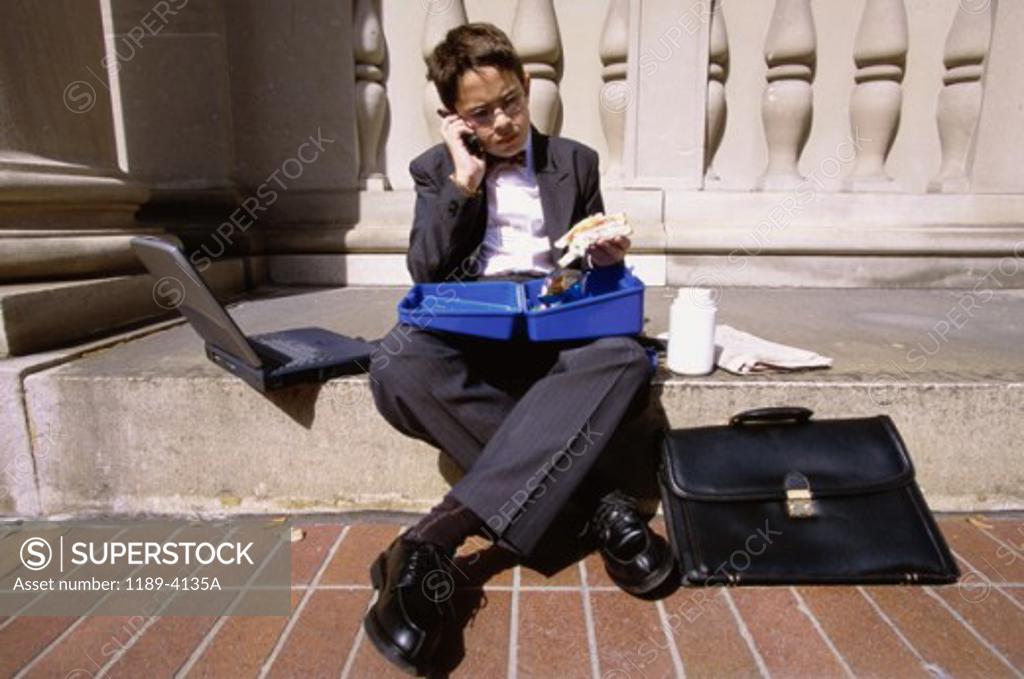 Stock Photo: 1189-4135A Boy wearing a business suit sitting on a step holding a lunch box