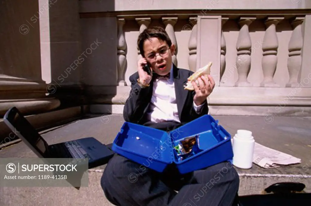 Boy wearing a business suit sitting on a step holding a lunch box