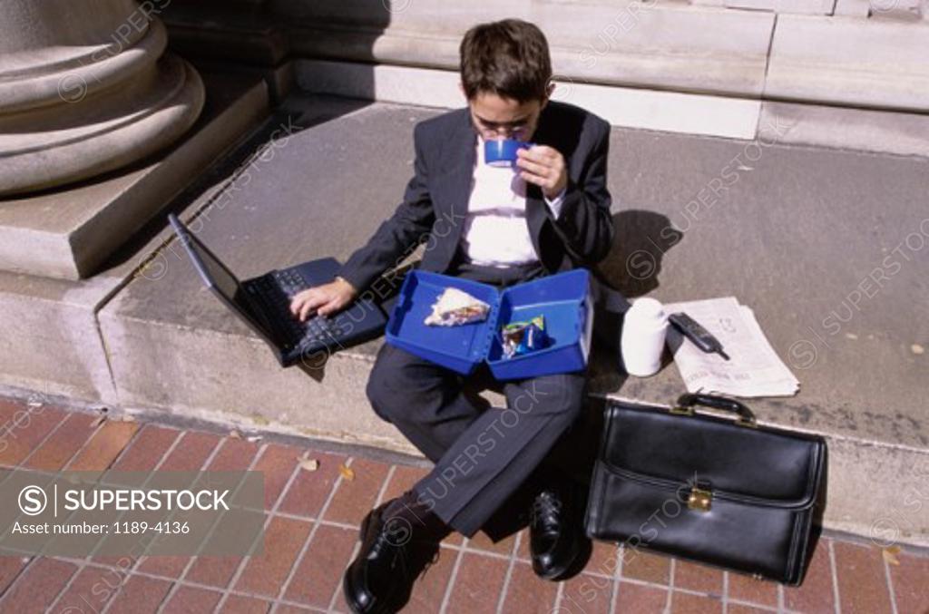 Stock Photo: 1189-4136 High angle view of a boy wearing a business suit sitting on a step holding a lunch box