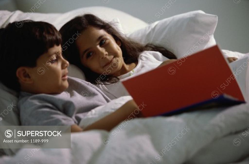 Stock Photo: 1189-999 Boy and a girl lying in bed reading a book