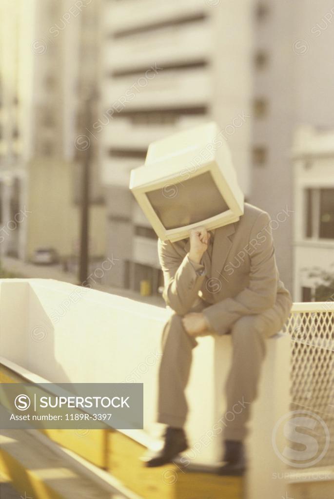 Stock Photo: 1189R-3397 Businessman sitting on a wall with computer monitor for a head