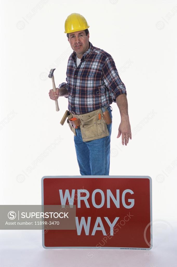 Stock Photo: 1189R-3470 Portrait of a worker holding a hammer standing next to a wrong way sign