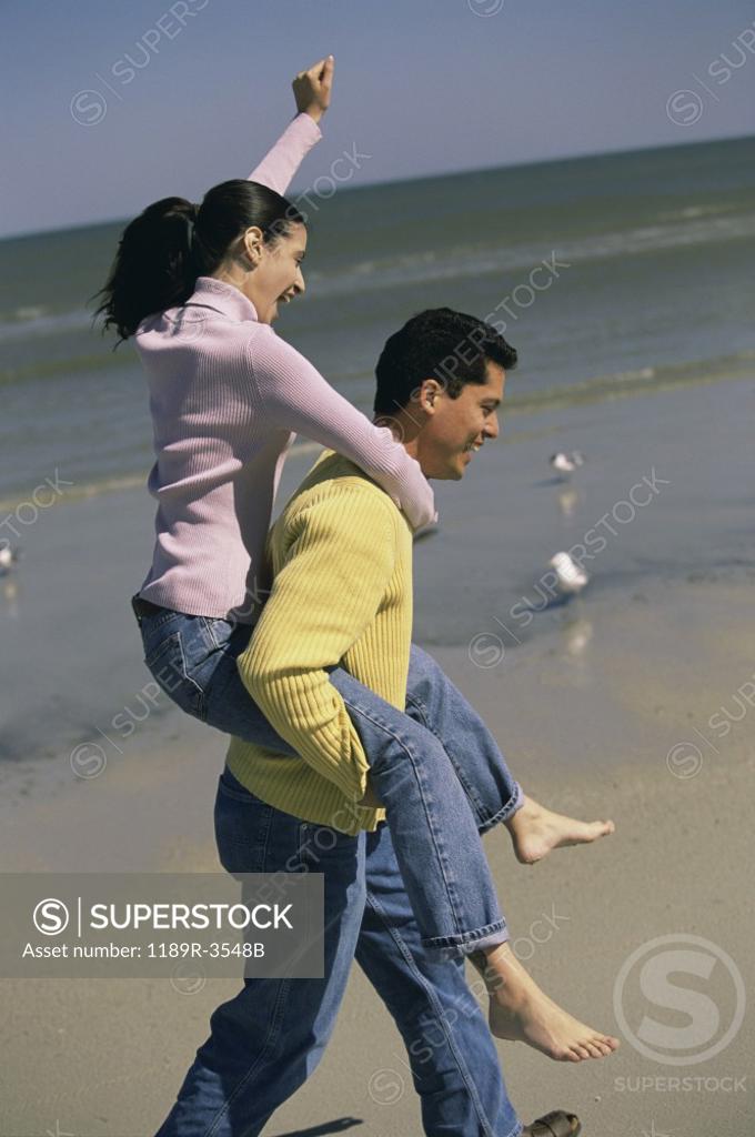 Stock Photo: 1189R-3548B Young woman riding piggyback on a young man at the beach