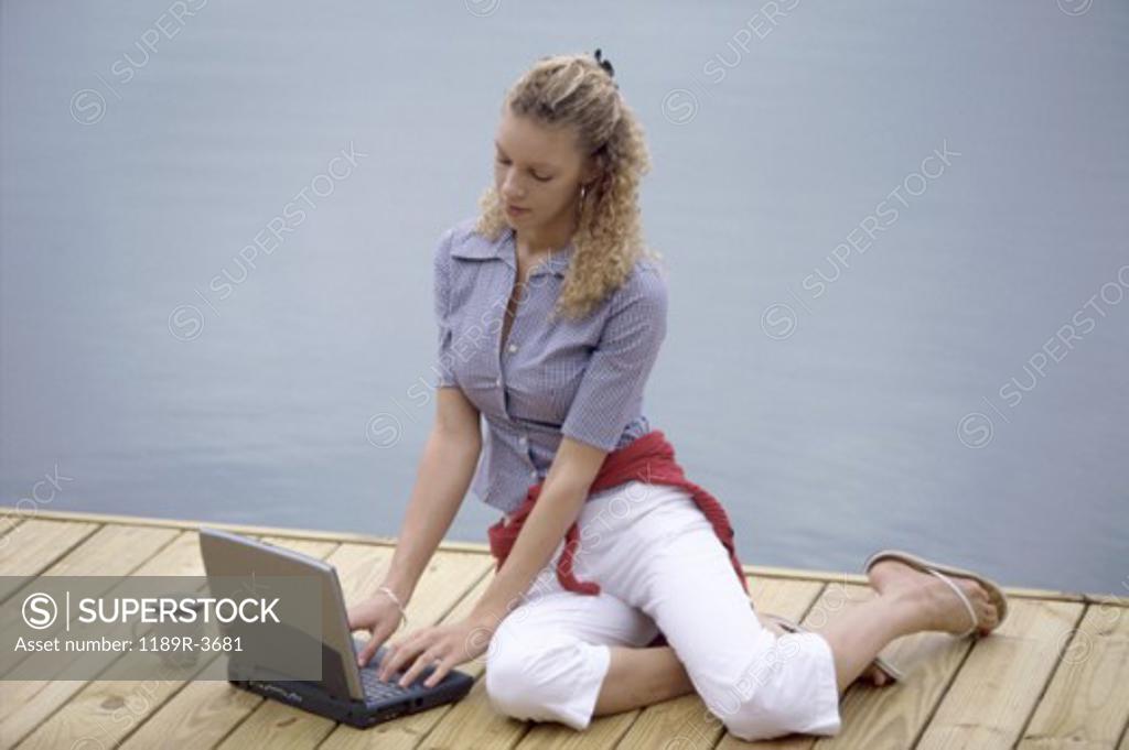 Stock Photo: 1189R-3681 Young woman sitting on a pier using a laptop