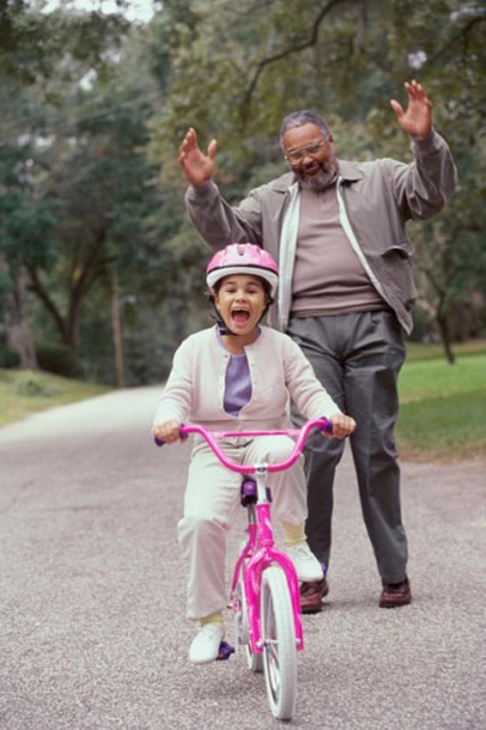 Girl riding a bicycle with her grandfather standing behind her