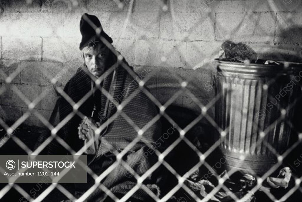 Stock Photo: 1202-144 Portrait of a mature man sitting on the street behind a chain link fence