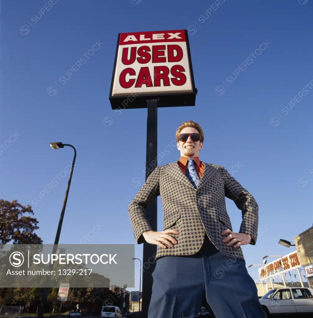 Low angle view of a car salesperson standing in front of a commercial sign