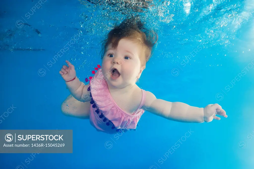 Little girl with an open mouth swimming underwater in the pool.