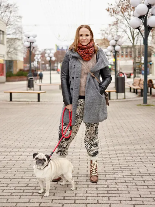 KERAVA, FINLAND - NOVEMBER 26, 2015: Young Woman holding a pug on leash, city view.