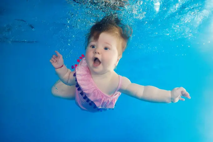 Little girl with an open mouth swimming underwater in the pool.