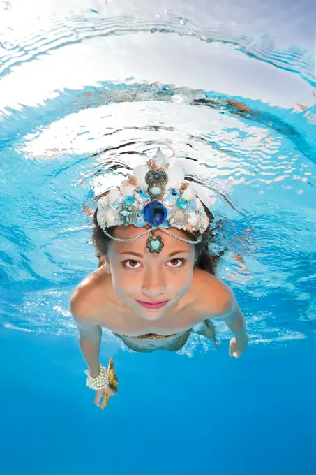 A girl in a mermaid costume poses underwater in a pool.