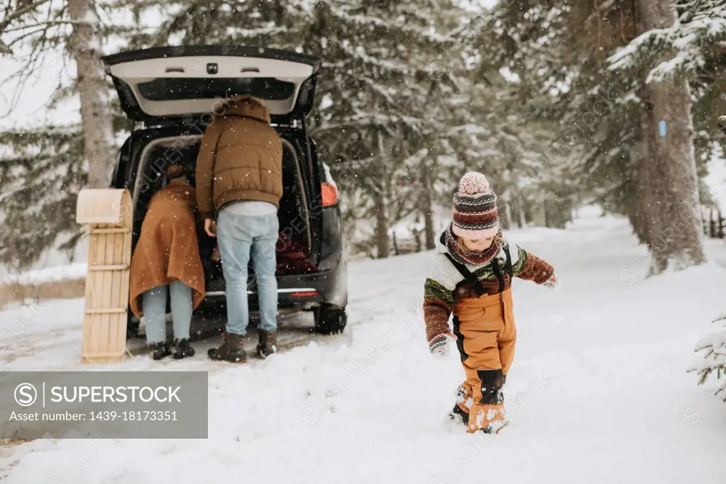 Canada, Ontario, Girl walking in snow and parents unpacking car trunk