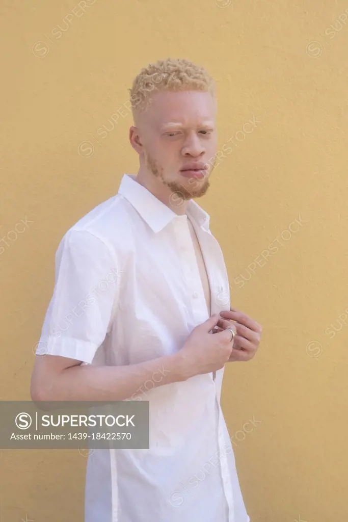 Germany, Cologne, Albino man in white shirt against yellow wall