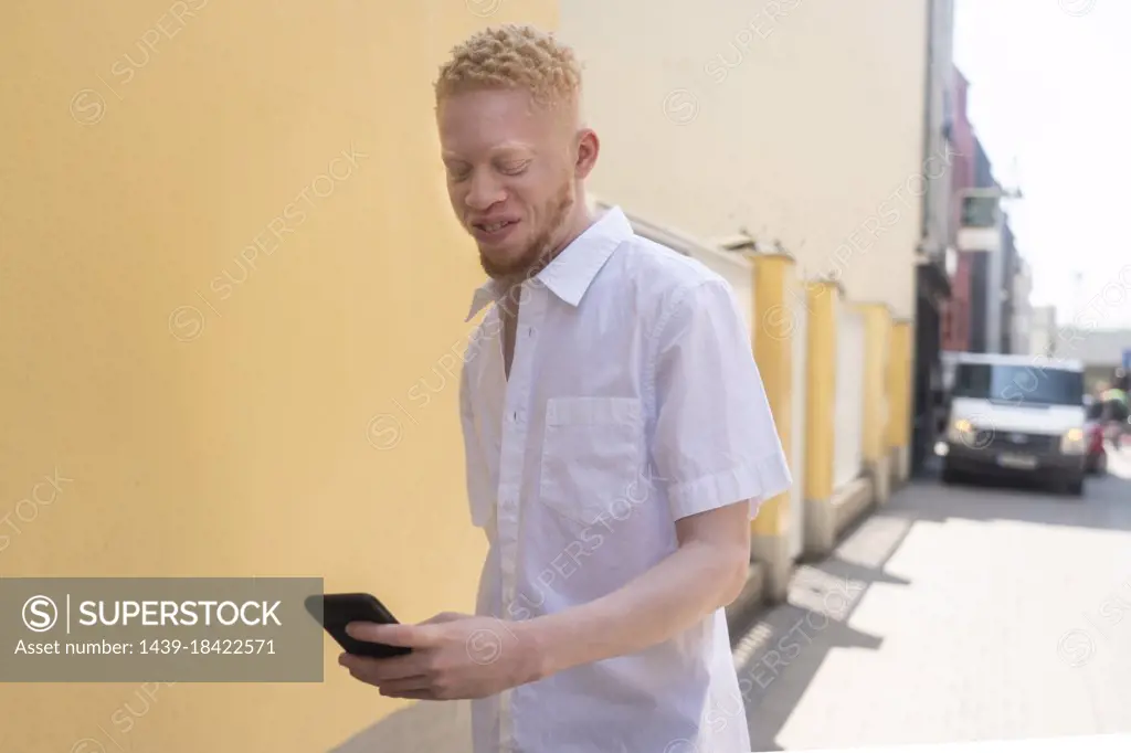 Germany, Cologne, Albino man in white shirt holding smart phone