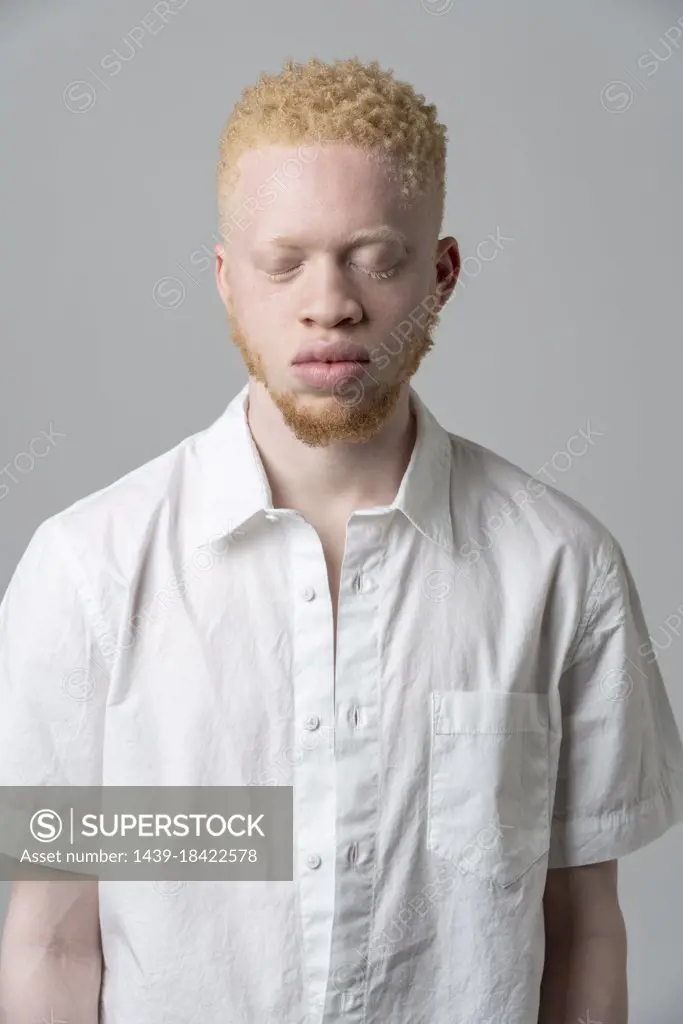 Studio portrait of albino man in white shirt with eyes closed