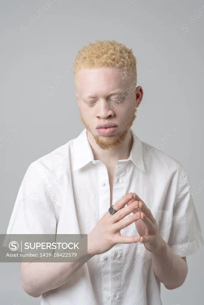Studio portrait of albino man in white shirt with eyes closed