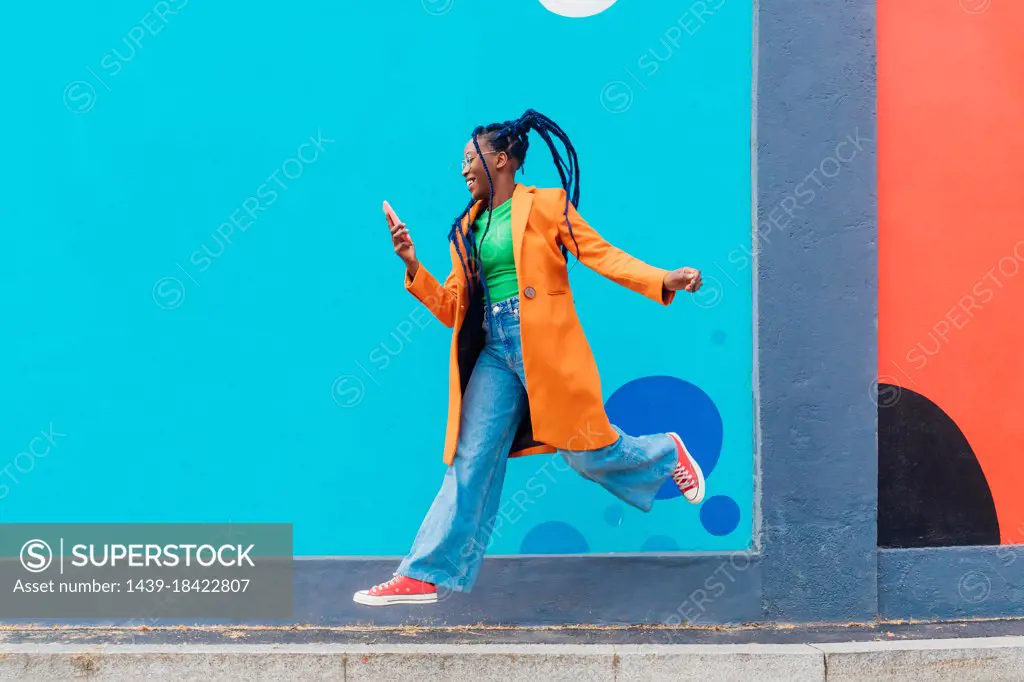 Italy, Milan, Woman with braids jumping against blue wall