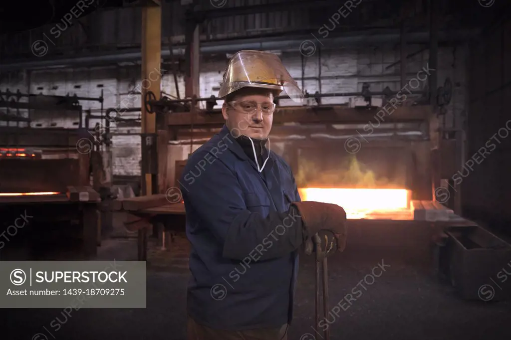 Forge worker, second in command of hammer control or "stamper" in pre forming forging area with a set of industrial tongs as furnace door is closed