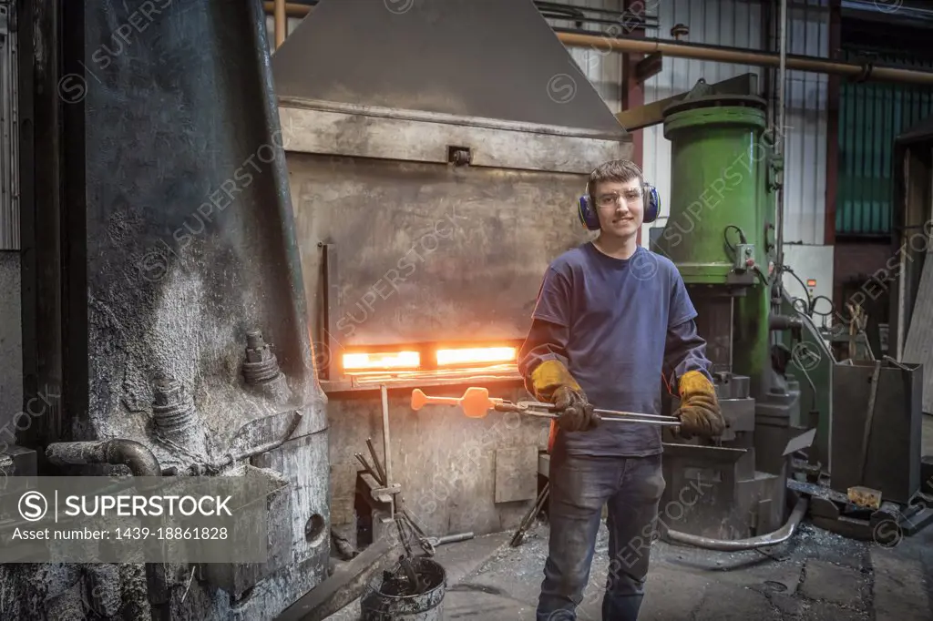 Portrait of apprentice engineer with hot titanium part in industrial forge