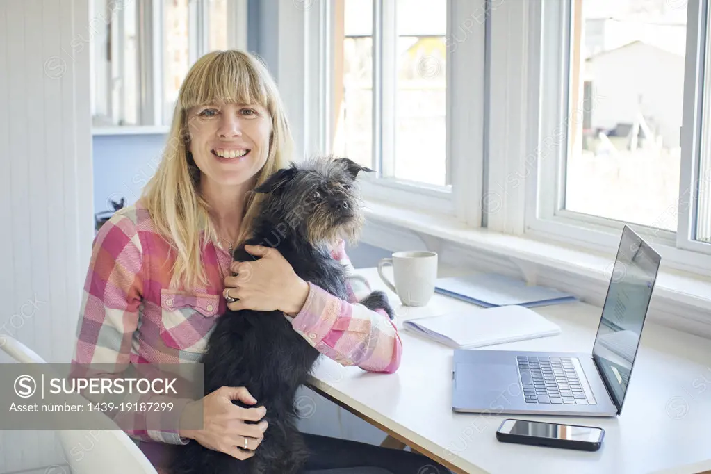 Portrait of mature woman holding dog and working from home