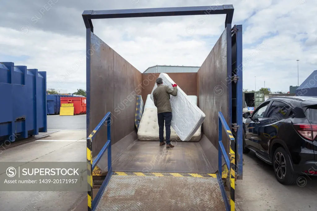 UK, Grimsby, Rear view of man unloading old mattresses at recycling center