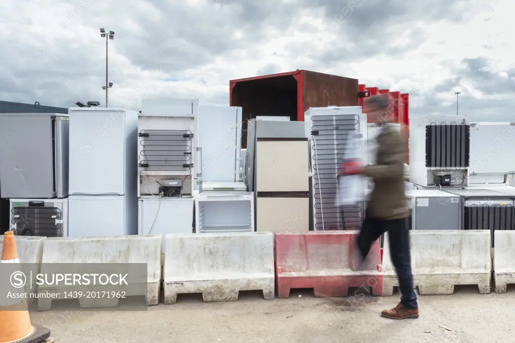 UK, Grimsby, Man passing by stacks of old refrigerators at recycling center