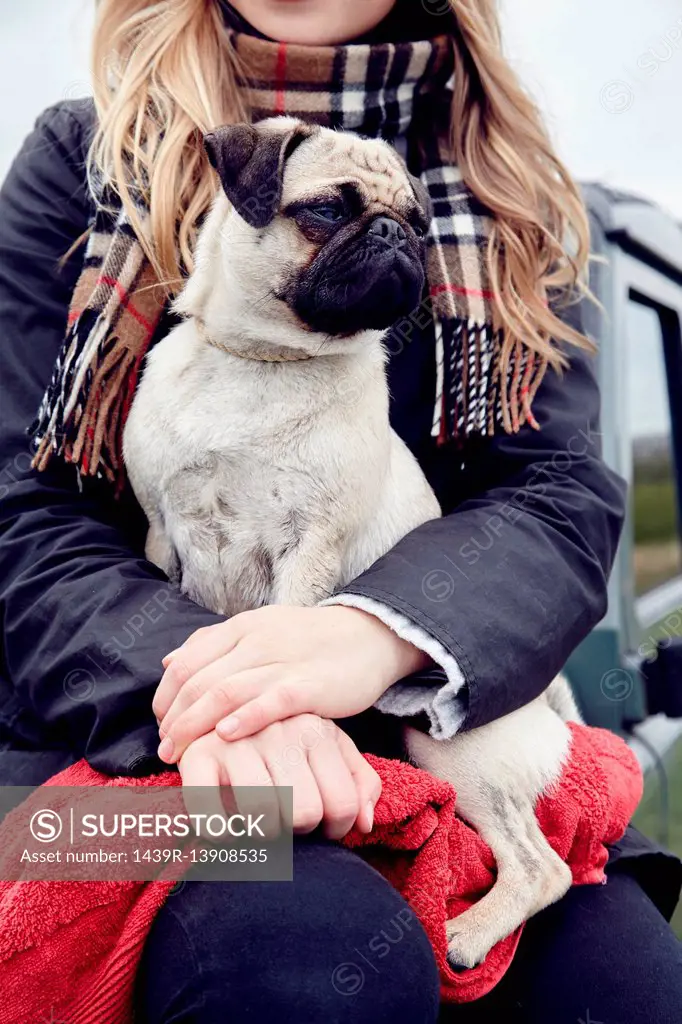 Mid section of young woman sitting on off road vehicle with dog on lap