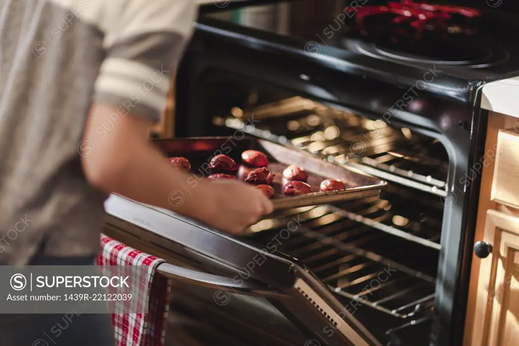 Girl placing tray of christmas cookies into oven, mid section