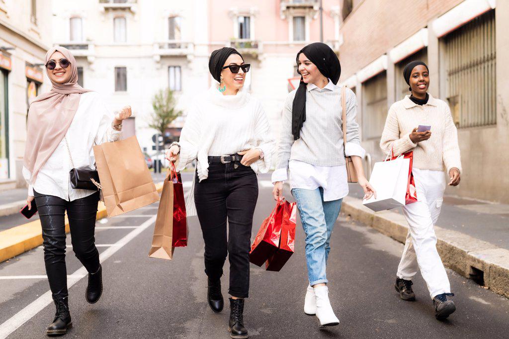 Four female friends walking along street with shopping bags