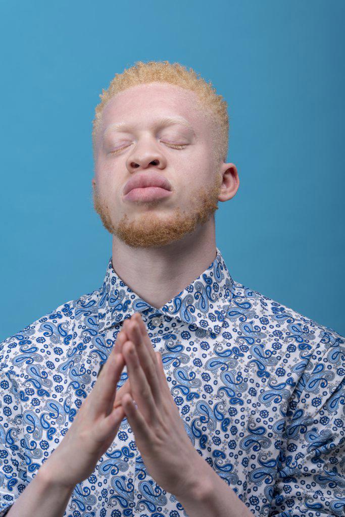 Studio portrait of albino man in blue patterned shirt with eyes closed