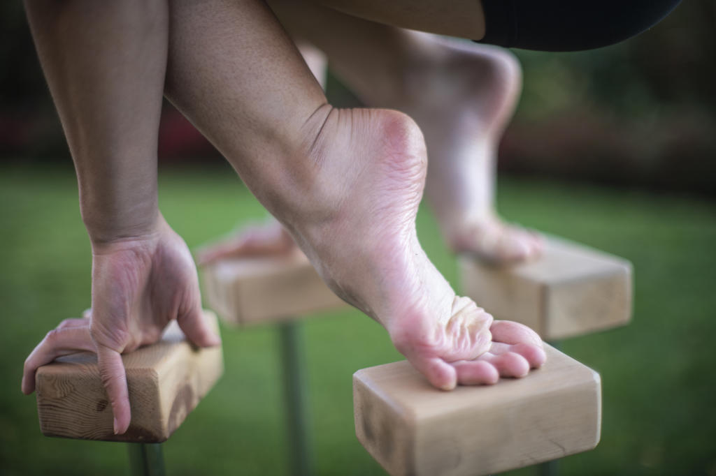 Close-up of foot and hand of female gymnast balancing on blocks outdoors