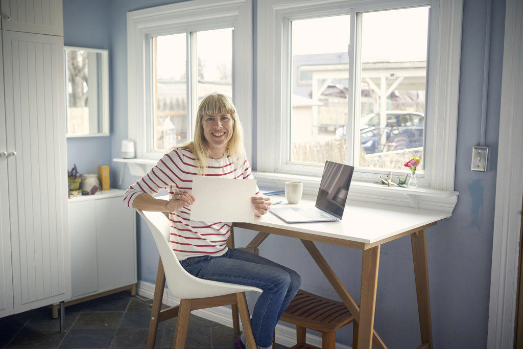 Portrait of smiling woman working from home and holding blank paper
