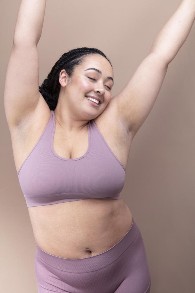 Studio shot of smiling woman in underwear with eyes closed and arms raised