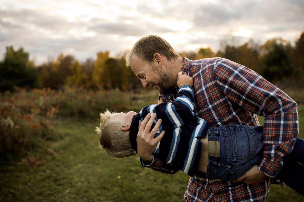 Father carrying son in arms playfully, face to face smiling