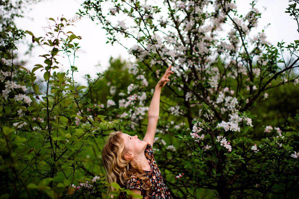 Girl with wavy blond hair reaching up to tree blossom