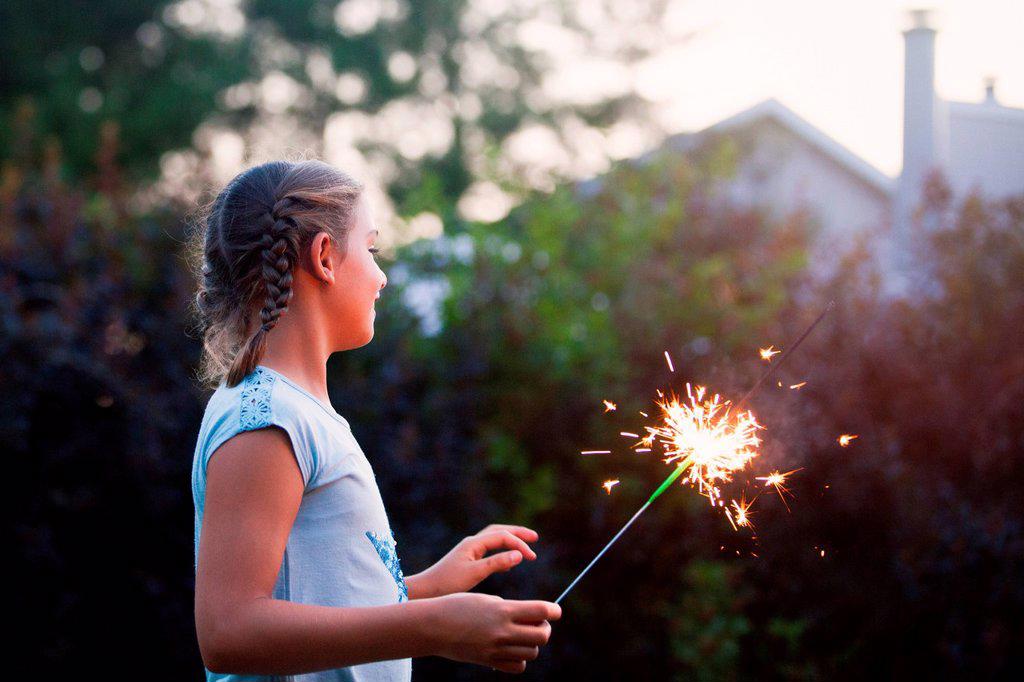 Girl holding sparkler in garden at dusk on independence day, USA