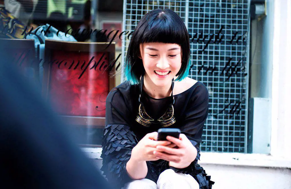 Young stylish woman sitting outside shop looking at smartphone