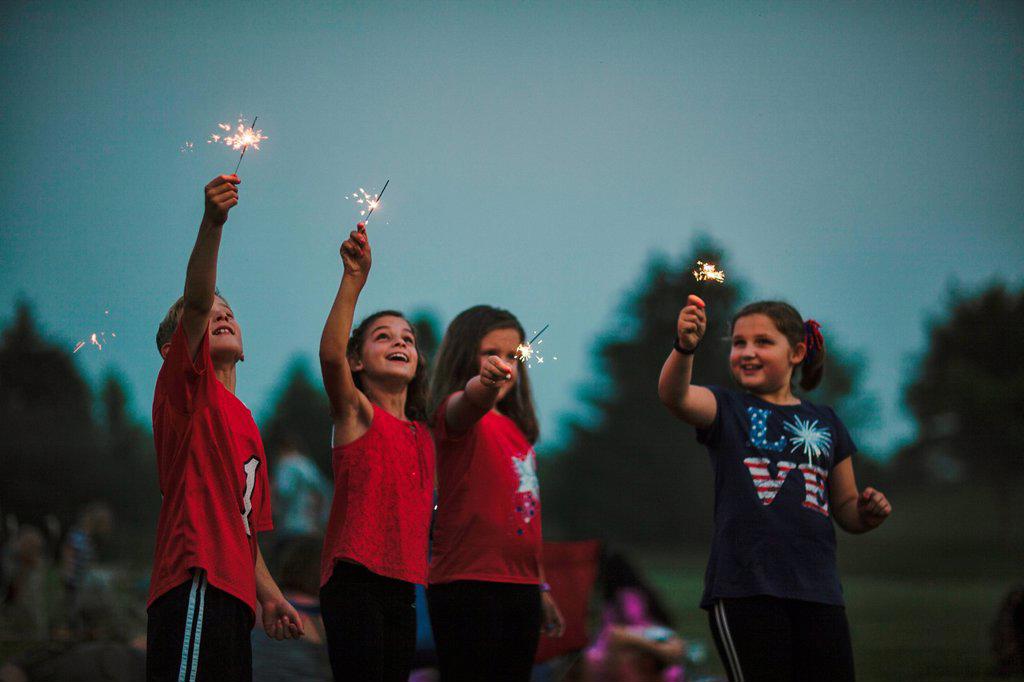 Group of friends, arms raised holding sparklers