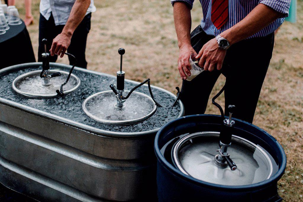 Men pouring beer from keg in cooling bath at barbecue, cropped