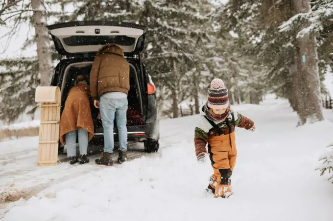 Canada, Ontario, Girl walking in snow and parents unpacking car trunk